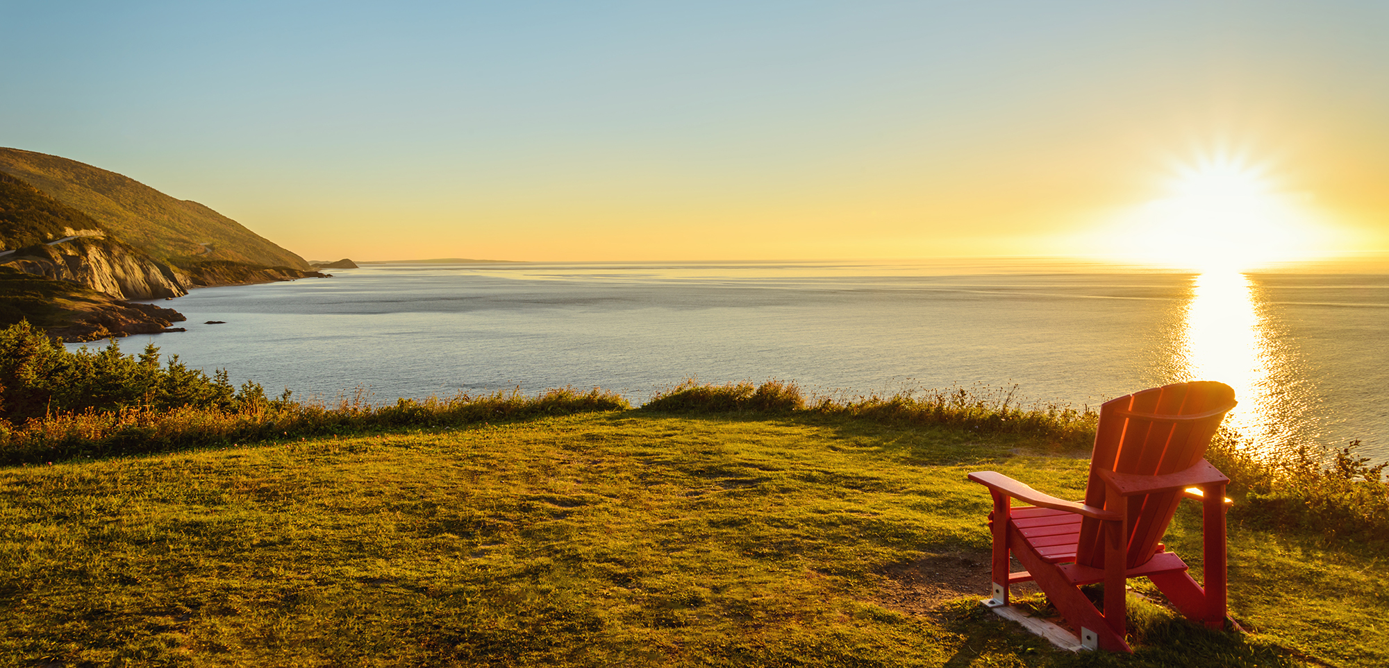 Red muskoka chair overlooking a sunset on a hill